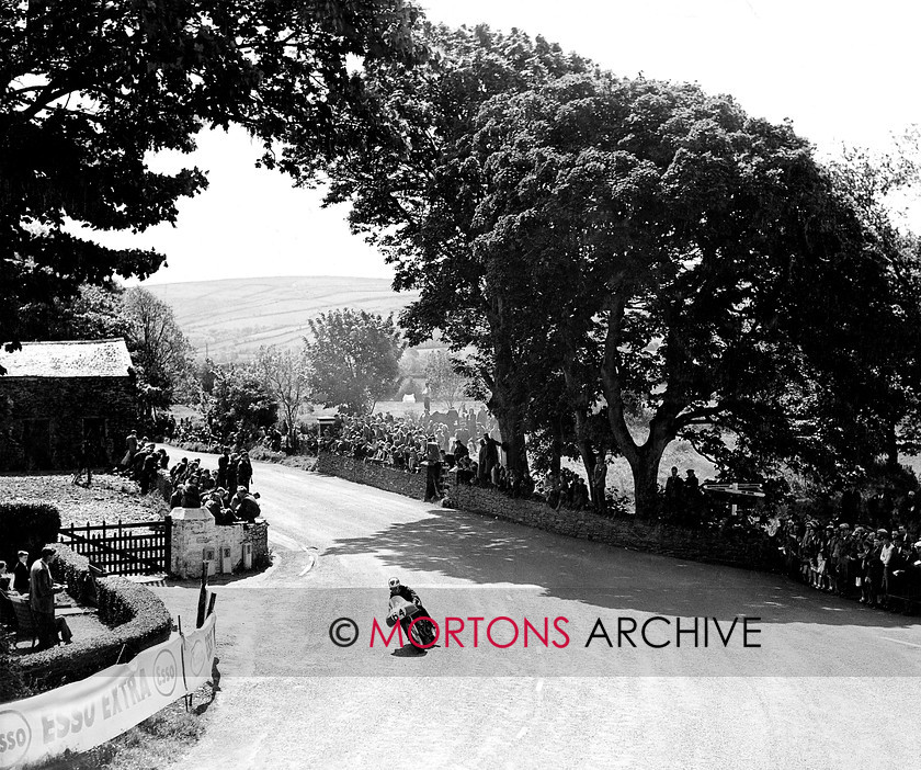 Manx 8B 
 8B – In this unusual view of Ballacraine Frank Fox tips his Norton into the right hander. 
 Keywords: 2012, Exhibition of historic images, Manx Grand Prix, Mortons Archive, Mortons Media Group, Mountain Milestones - Memories from Mona's Isle
