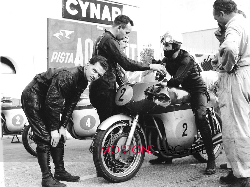 MV 05 
 The dominant two Johns, Hartle (on bike) and Surtees (standing) with journalist Vic Willoughby peering at the camera. 
 Keywords: Mortons Archive, Mortons Media Group, MV